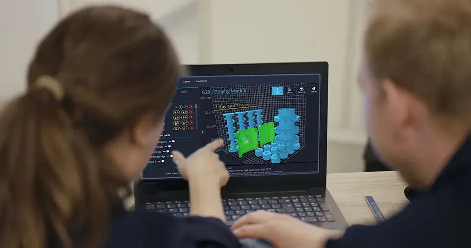 2 people looking at a computer monitor showing a part queue