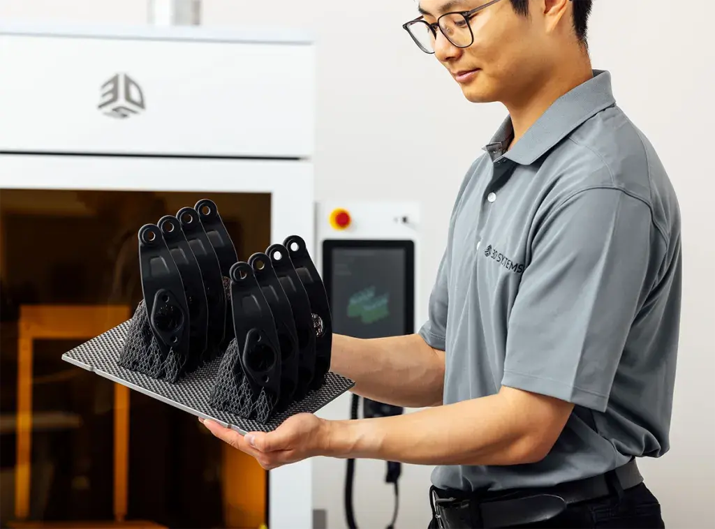 A man standing at a 3D printer holding a tray of 3D printed parts